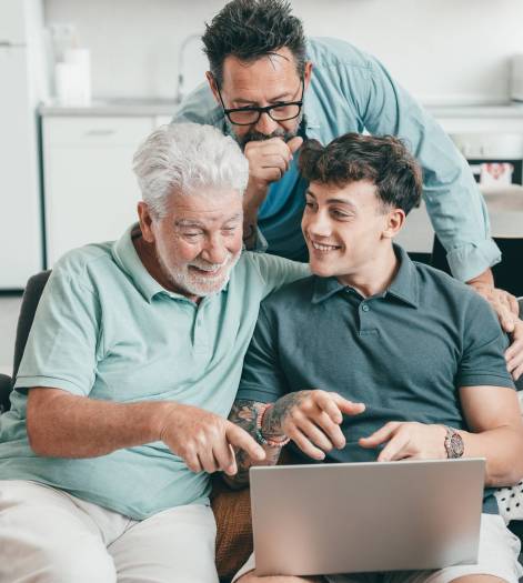 Happy grandfather learning new computer technology from young grandson, handsome smiling boy teaching father and grandfather how to use computer, shop online, book travel and vacation